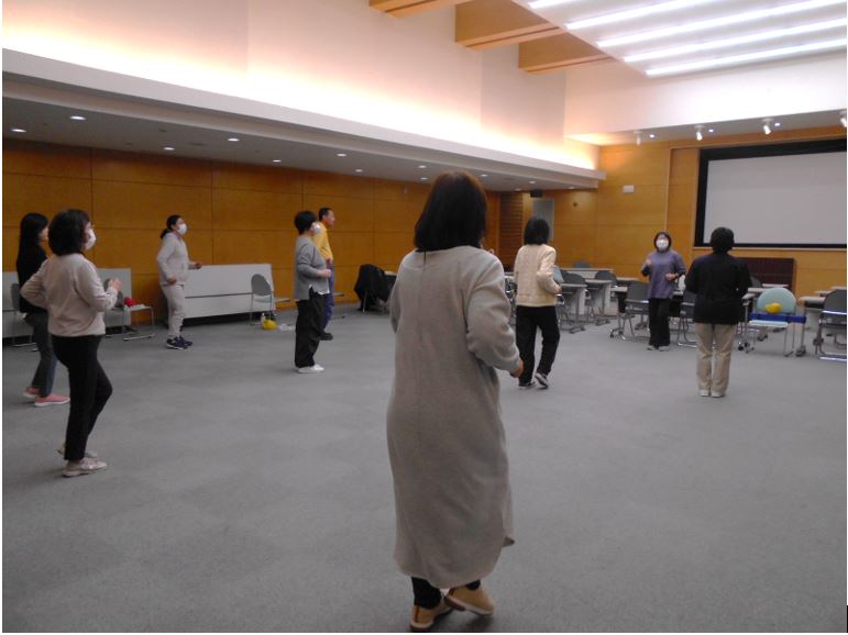広い会場で間隔をあけて立った参加者たちが運動をしている様子の写真