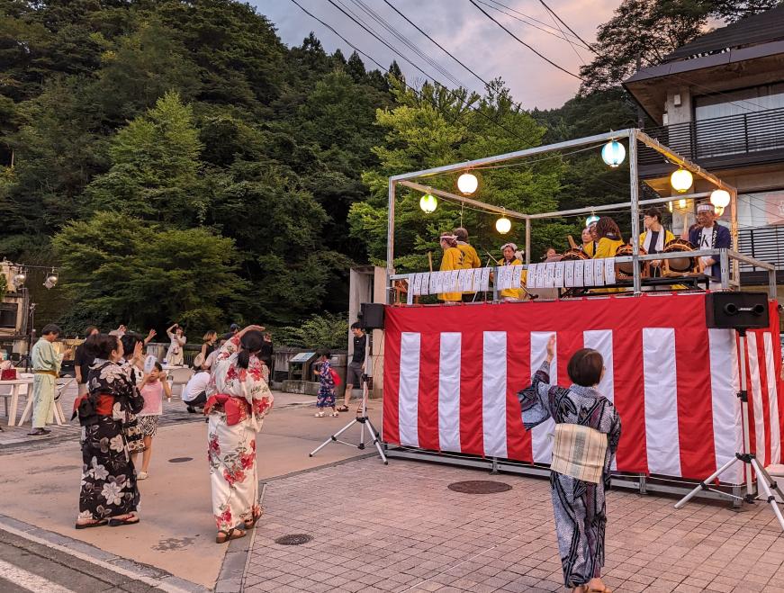 舞台の上の和太鼓の演奏に合わせて浴衣姿の女性が土湯盆踊りを楽しむ写真
