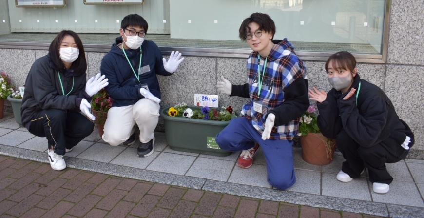 花植えされたプランターの横に4名の男女が座り記念撮影している写真