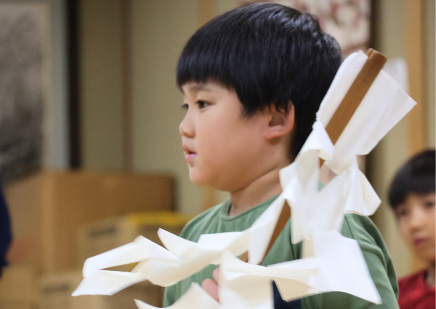 緑色の服を着た男の子が紙垂がついたお祓い棒を持ち真っすぐ前を見ている写真