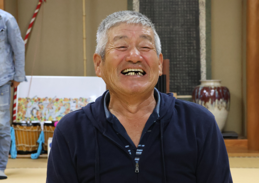 紺色の服を着て笑っている佐藤会長をアップで撮影した写真