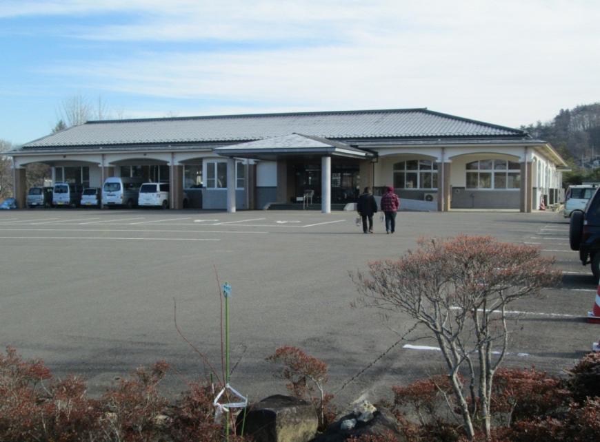植栽のある広い駐車場の奥に建っている1階建ての福島市飯野地域福祉センターの外観写真