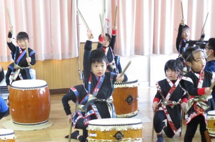 半被を着た子どもたちが和太鼓の前でばちを振り上げて、和太鼓の演奏を披露している様子の写真