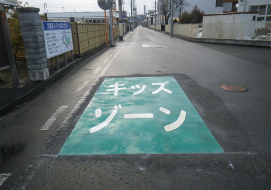 道路の一部分が緑色で塗られ、白い文字で大きくキッズゾーンと書かれた福島敬香保育園前のキッズゾーンの写真