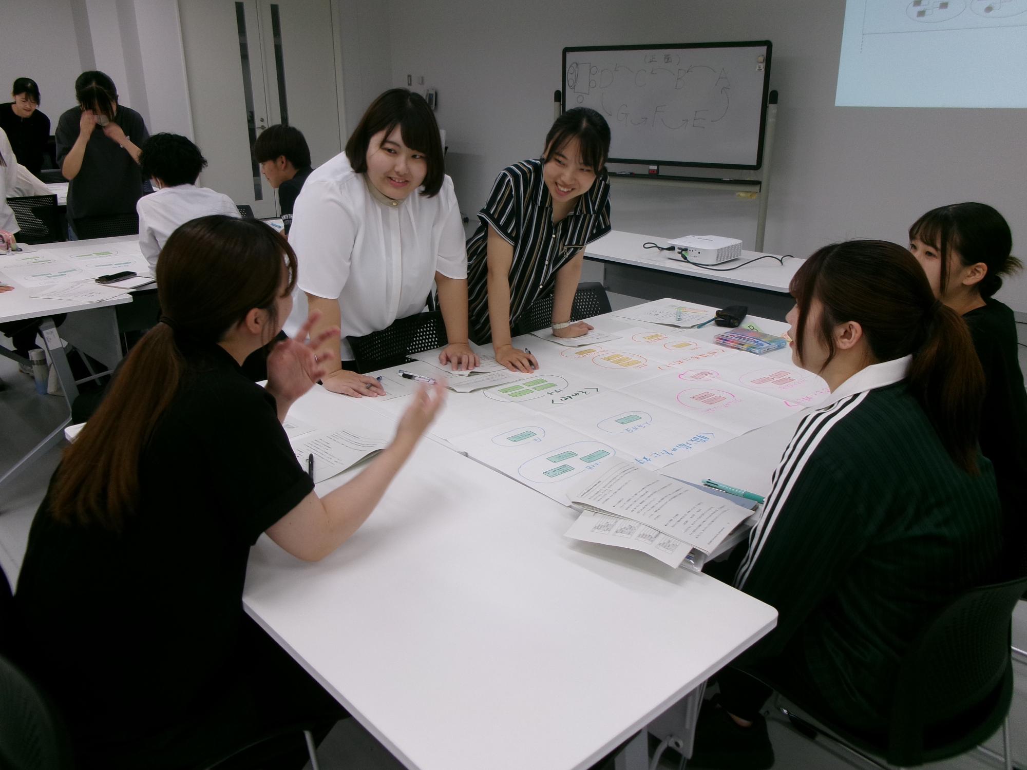 模造紙を広げたテーブルを囲んで座った参加者たちがペンを持って模造紙に書き込んでいる様子の写真