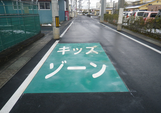 道路の一部分が緑色で塗られ、白い文字で大きくキッズゾーンと書かれたたんぽぽ第二保育園前のキッズゾーンの写真