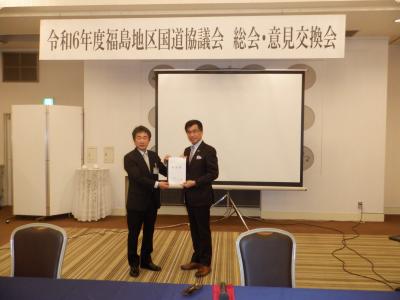 令和6年度福島地区国道協議会 総会・意見交換会と書かれたボードの前で、鈴木由起彦土木部次長と福島市長が要望書を持ち記念撮影をしている写真