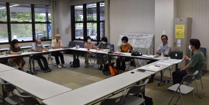 ロの字型に設置した長机の席に座った参加者たちが打ち合わせを行っている様子の写真