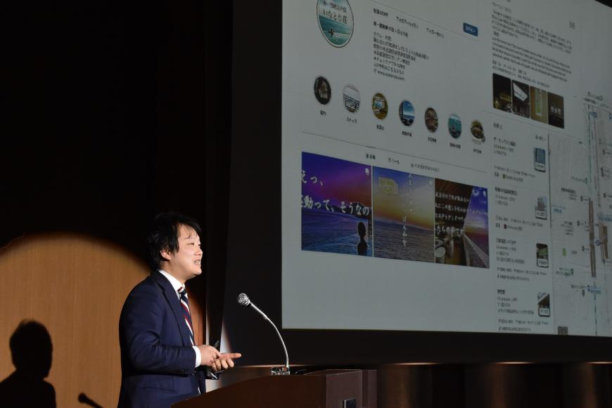 資料が映し出されたスクリーンの右側の檀上に立つ渡邉氏が話をしている様子の写真