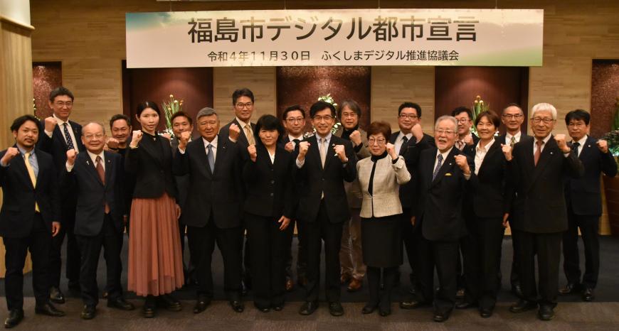 「福島市デジタル都市宣言」と書かれた横断幕の下で、市長を中央に関係者がガッツポーズをして並んでいる写真