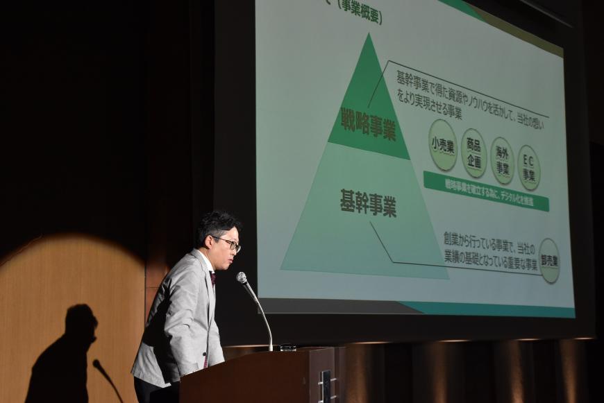 資料が映し出されたスクリーンの左側の檀上に立つ渋谷氏が話をしている様子の写真
