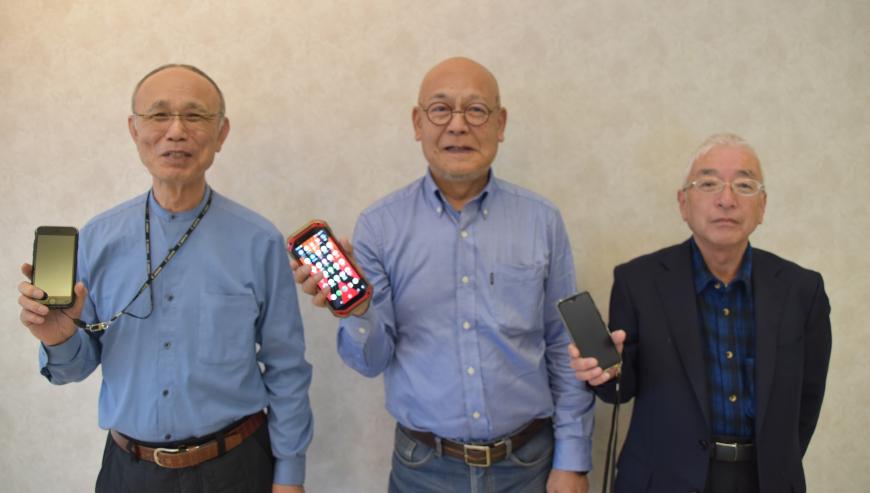 それぞれスマートフォンを右手に持った3名の男性が横一列に並んでいる写真