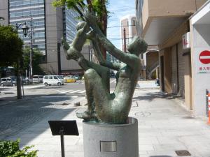 母親が幼児を自分の足に乗せ両手で抱きあげている作品「遊ぶ」の写真