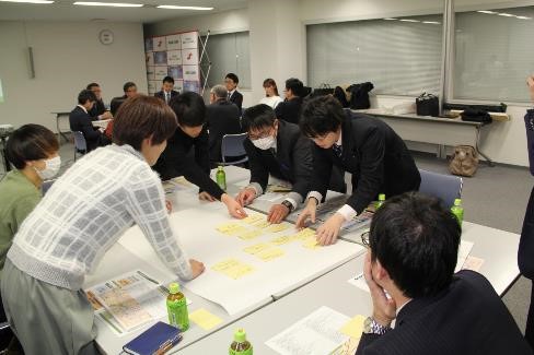 参加者の人たちが机に置かれた紙に付箋を貼りながら話し合いをしている写真
