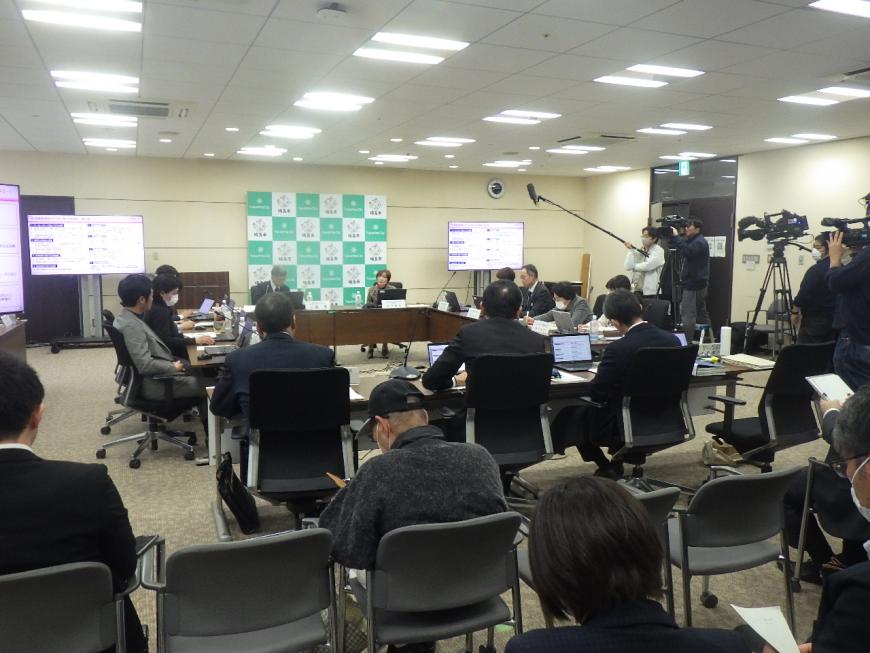 中央にはロの字で並べられた長机に関係者が座り、右横には撮影スタッフの人たちが並んでいる第7回会議の様子の写真