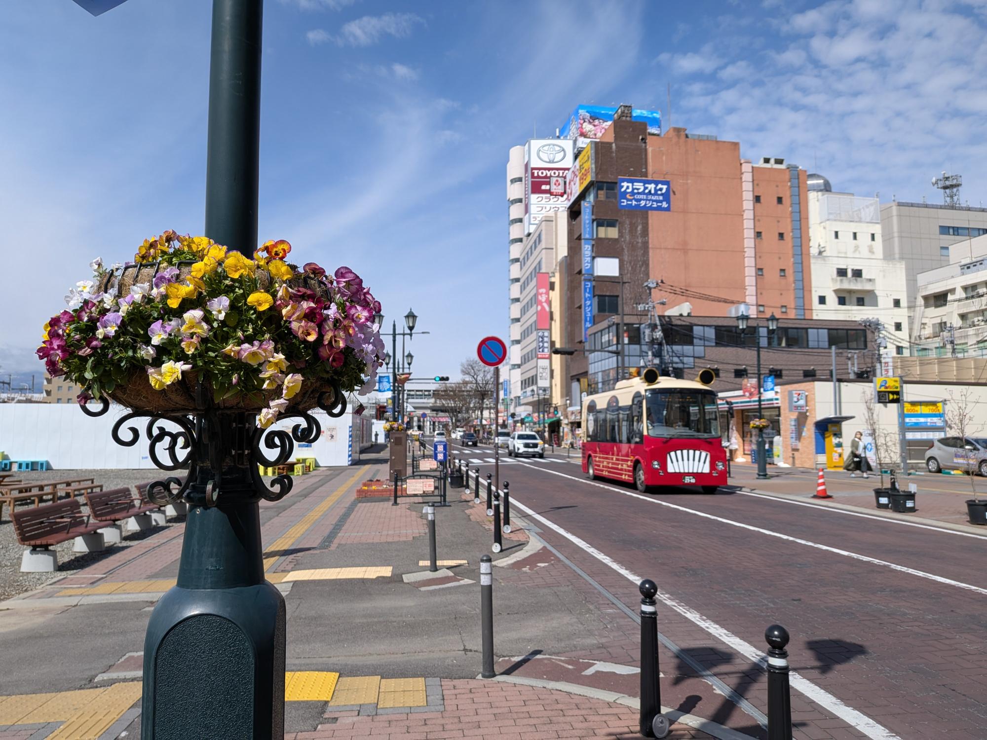 街灯のフラワーバスケットに黄色や紫、白の花々が咲いている写真