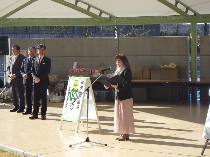 開園150周年と書かれた看板の横で女性がマイクの前で話をしている様子の写真