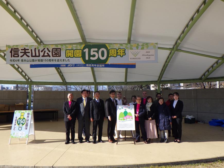 信夫山公園開園150周年と書かれた横断幕を背景に関係者が2列に並び記念撮影を行っている写真