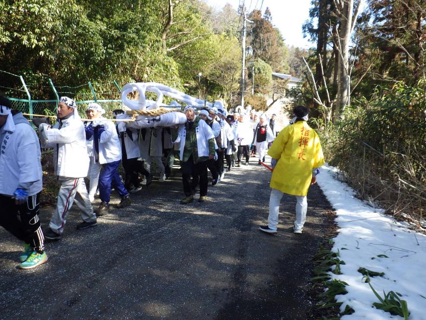 大わらじを白い半被を着たたくさんの関係者が肩に担いで道路を歩いている様子の写真
