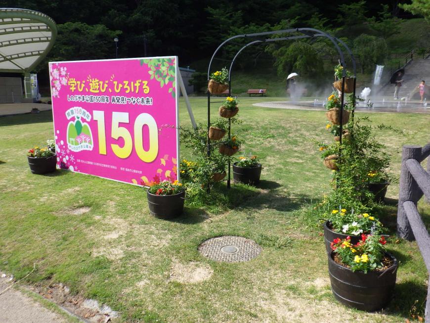 信夫山公園開園記念の大きな看板の近くを大小様々なプランターで装飾している広場の写真