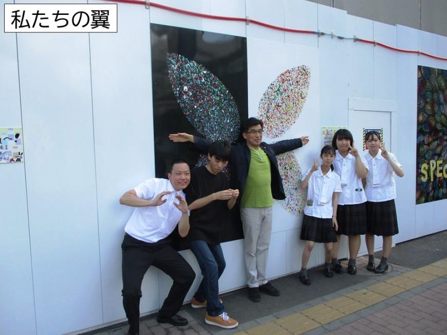 蝶の羽のようなアートの前で6名の人たちが各々ポーズをとっている写真