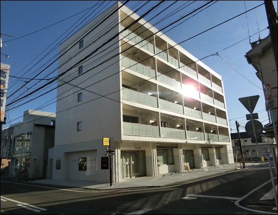白い外壁で5階建て、2階以上が住居、1階が店舗になっている建物の外観写真