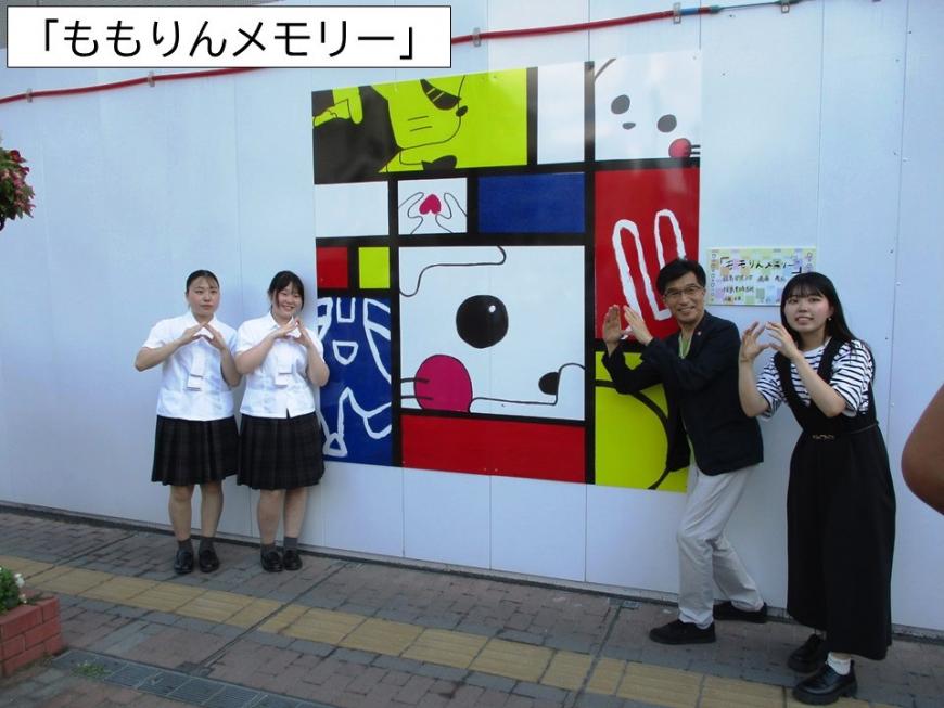 ももりんメモリーのアート作品の前で両手で三角をつくった4名の人たちが記念撮影をしている写真
