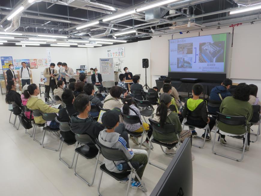椅子に座った参加者の人たちが正面のモニターを見ている見学会の写真