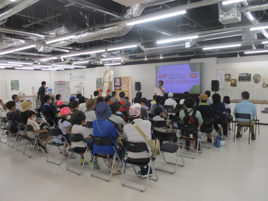見学会でモニターの前で男性が説明をしている様子を参加者の人たちが椅子に座り聞いている写真
