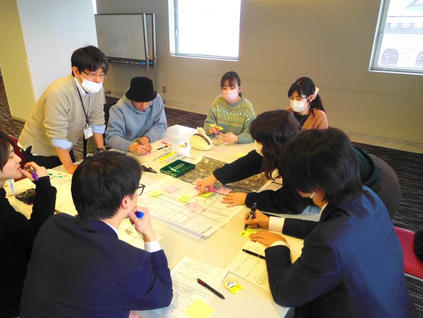 テーブルの上に広げた資料を指さしながら話し合いをしている参加者の写真
