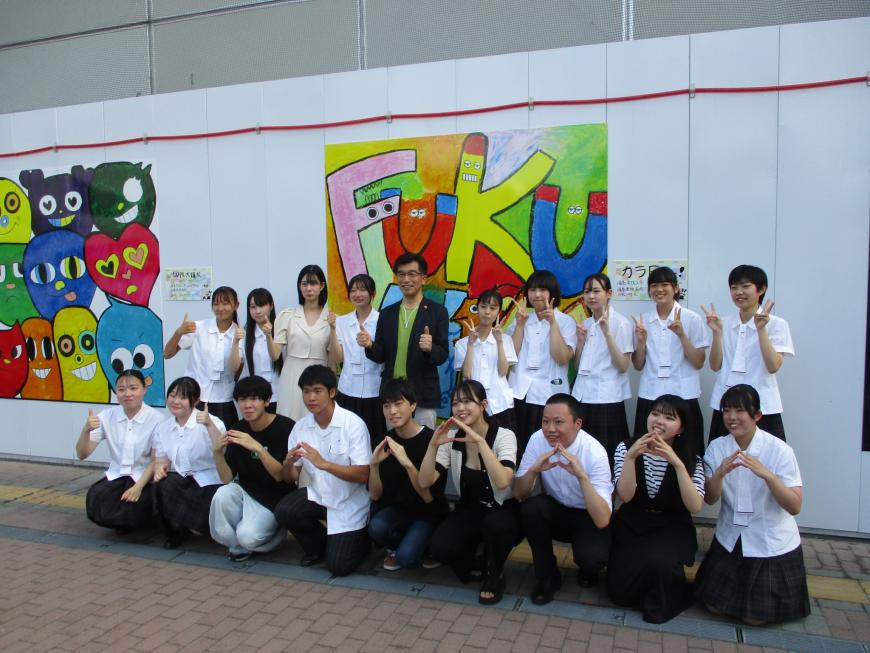 FUKUのスプレーアートの前で男女の学生が2列に並んでピースサインをしている写真