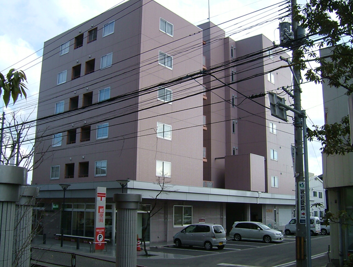 茶色い外壁で1階に郵便局が入っており駐車場に車が停まっている建物の外観写真