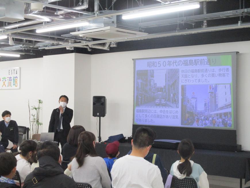 昭和50年代の福島駅前通りのモニターを見せながら説明をしている男性と椅子に座り聞いている参加者の人たちの写真