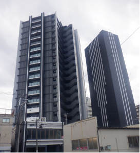 グレーの外壁で右側に外階段が設置されている19階建ての高層マンションの写真