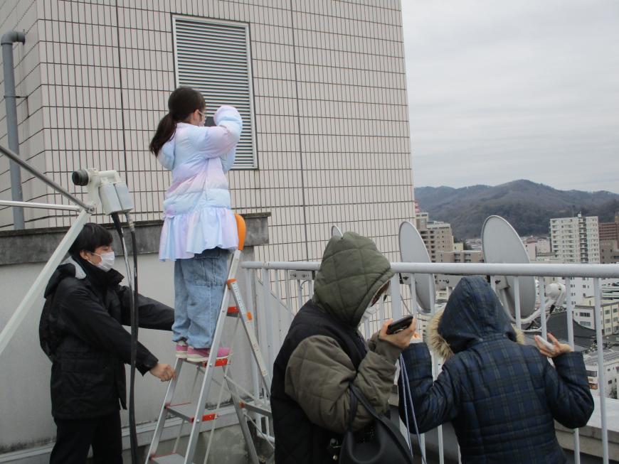 屋外で三脚に乗って女の子が風景を撮影している様子の写真