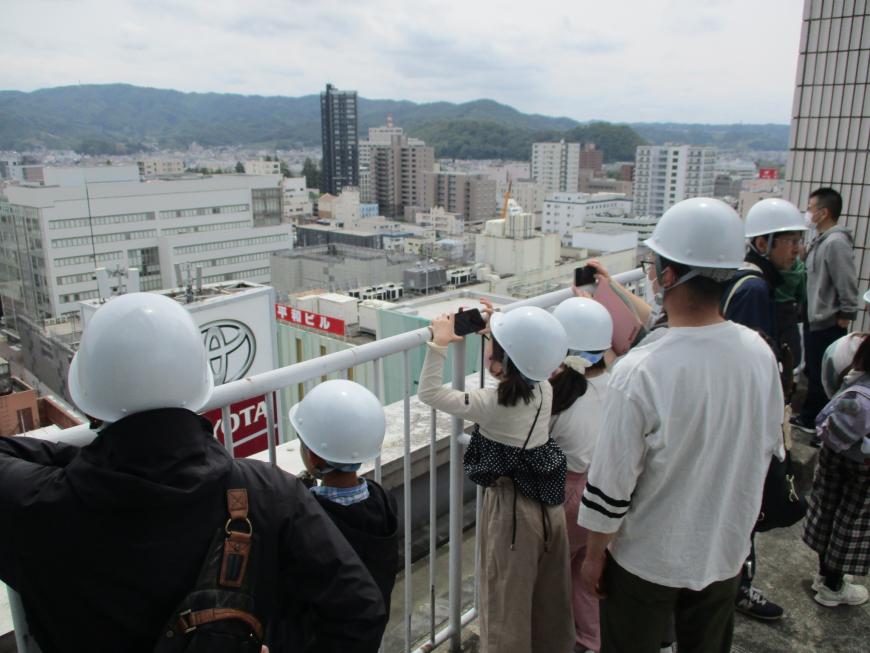 白いヘルメット着用した参加者の人たちが各々スマホなどで工事現場を撮影している写真