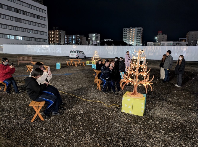 暗闇の中、木で作られたツリーをライトアップしスマホで写真を撮っている参加者の人たちの写真
