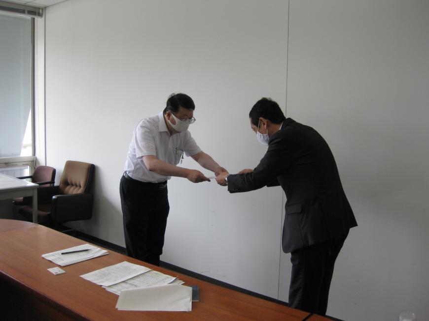 初澤会長と関係者の男性がお辞儀をしながら諮問書の受け渡しをしている写真