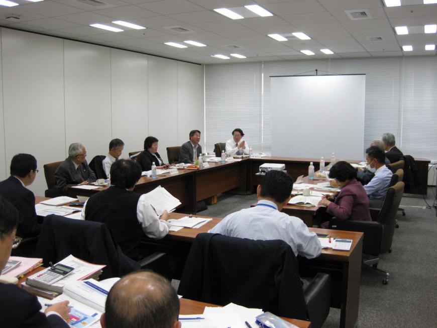 関係者の方々がロの字型に設置された長机の席に着き、資料に目を通しながら会議が行われている様子の写真