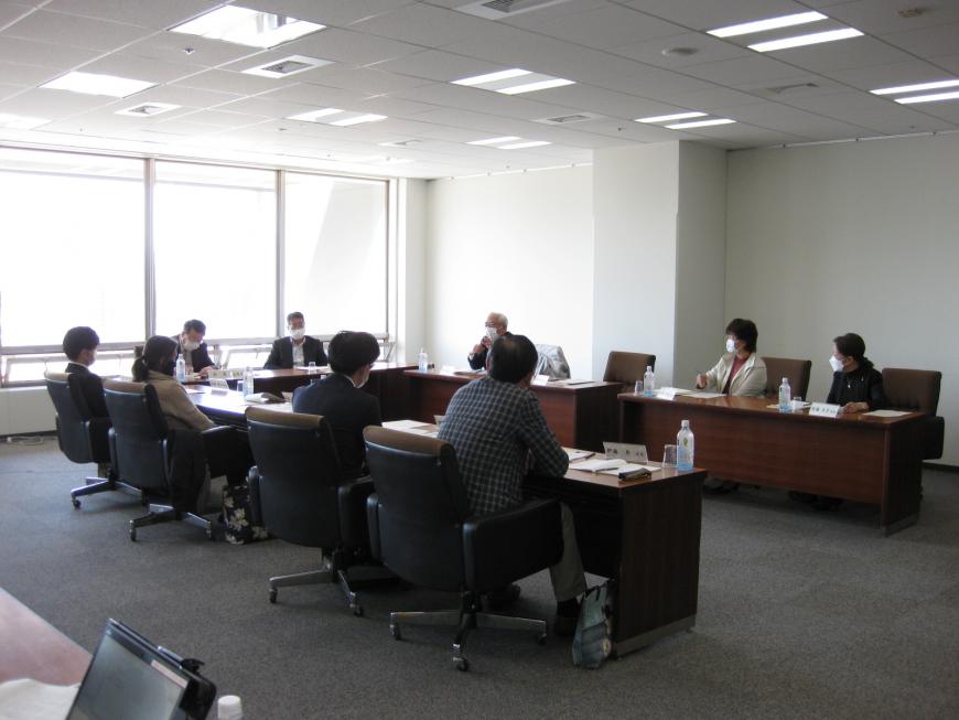 コ型に長机が並べられ関係者の人たちが席に座っている審議会の写真