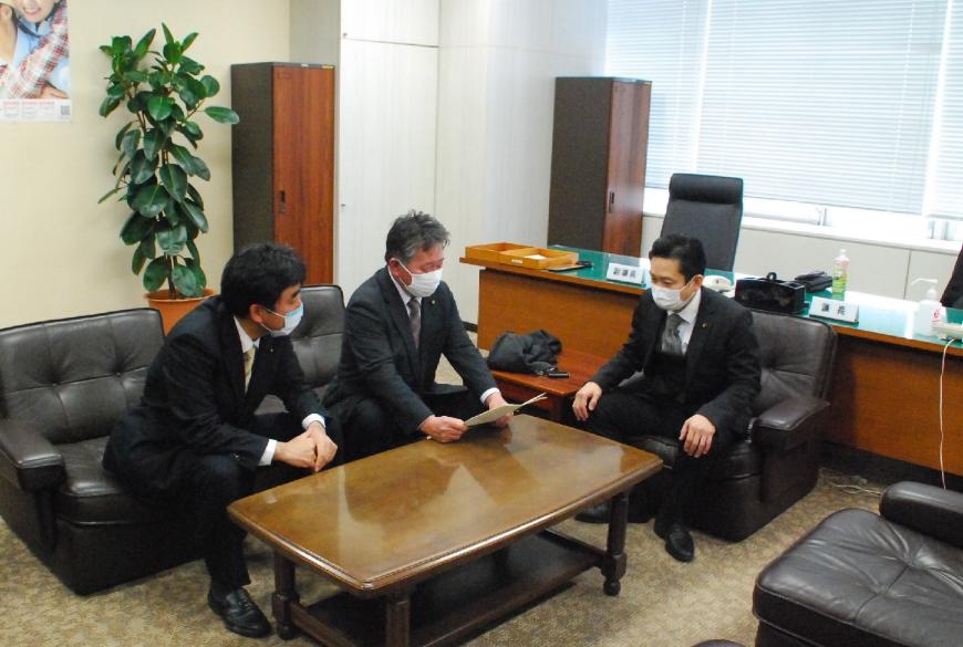 黒沢座長が答申書を手に持ち、石原副座長より真田議長と一緒に話をしている様子の写真
