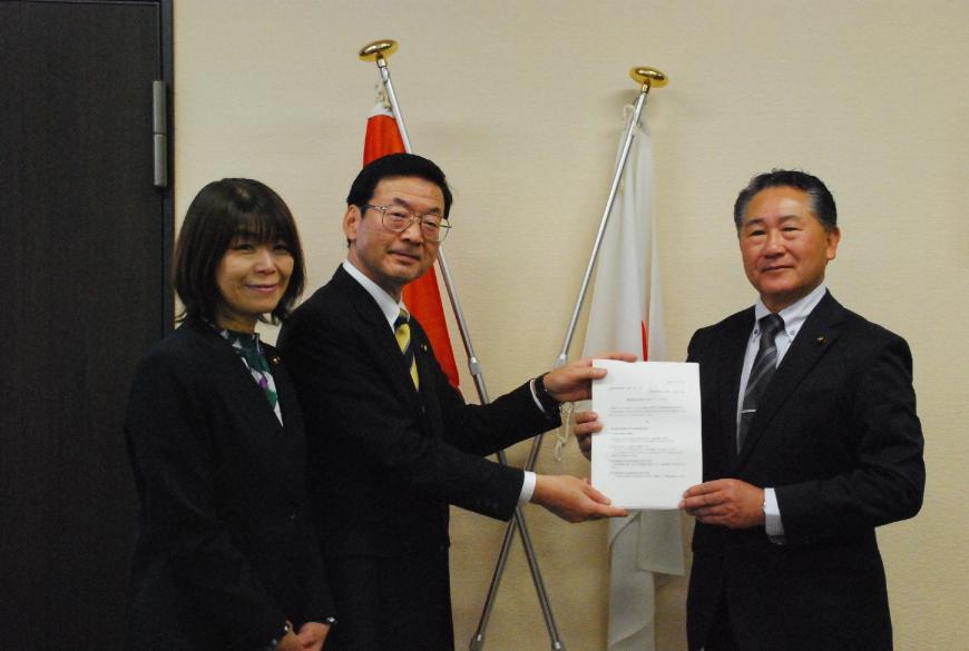 二階堂座長と萩原議長が一緒に答申書をカメラの方に向け持ち、二階堂座長の横には石山副座長が立ち記念撮影している写真