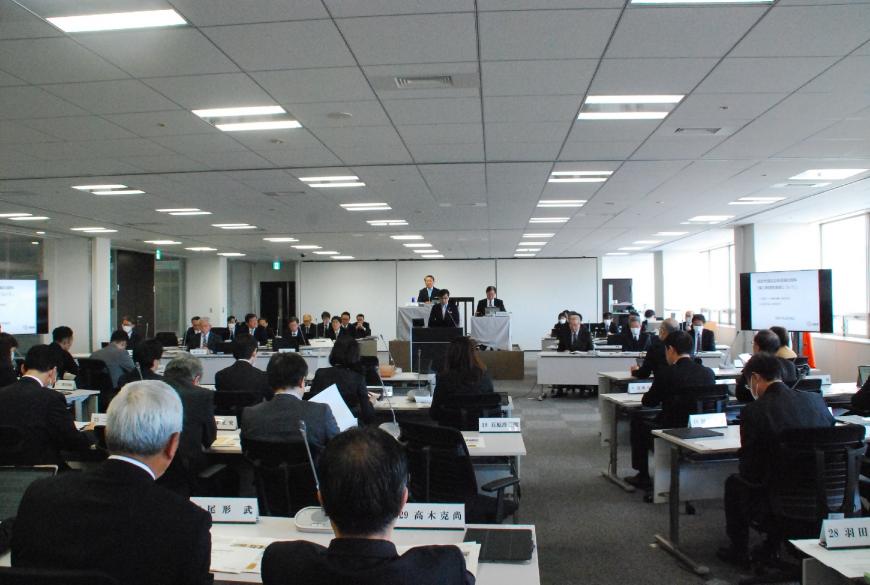 協議会に参加された関係者の方が設置されて席に座り、前方の演台に立つ男性の話を聞いている様子を後方から写した写真