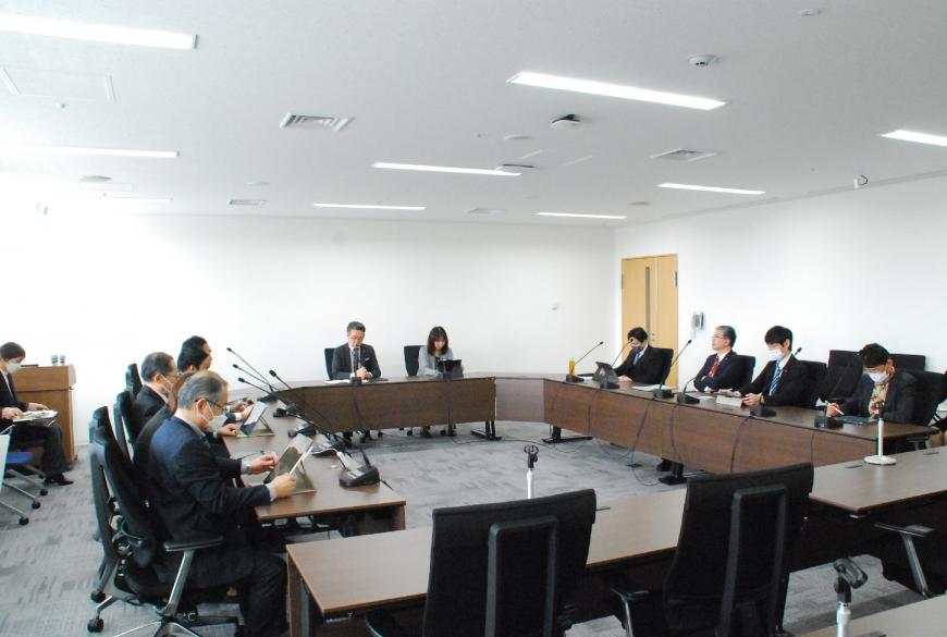 会議室で、ロの字型の会議テーブルの席に関係者らが座り、タブレットなどを見ながらを協議を行っている様子の写真