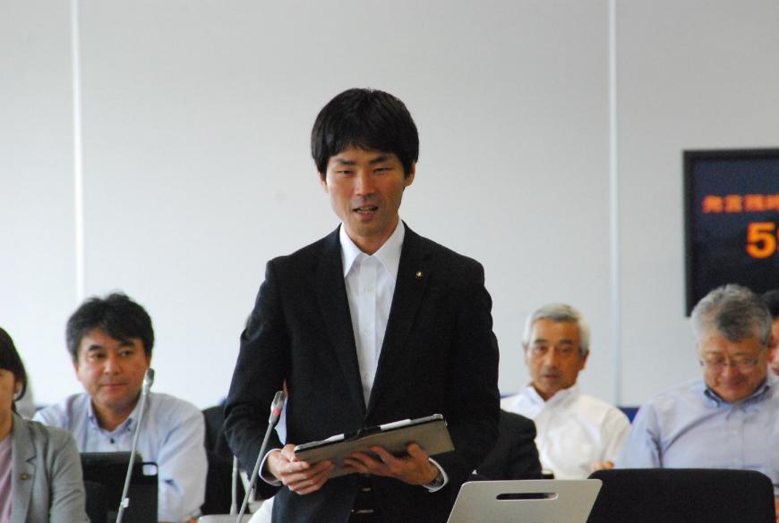 タブレットを持ち鋭い眼光で話をする根本雅昭議員を撮影した写真