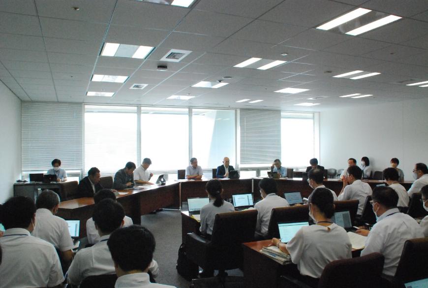 大きな窓から日の光が差し込む会議室で大勢の職員や役員が会議をしている様子を全体的に撮影した写真