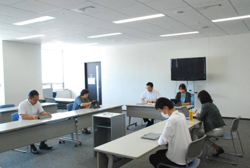 窓から光が差す会議室で6人の職員が会議をしている様子を撮影した写真