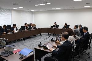 委員11名がコの字型に並べられた机に座り、タブレットを見ながら協議している写真。
