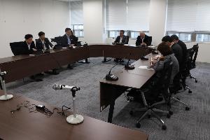 委員8名がコの字型に並べられた机に座り、タブレットを見ながら協議している写真。