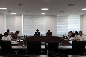 委員9名がコの字型のテーブルに座り、タブレット端末を見ながら協議している写真